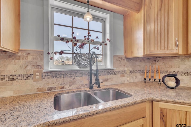 kitchen featuring pendant lighting, sink, backsplash, and light stone countertops