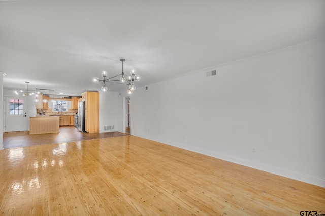 unfurnished living room with crown molding, an inviting chandelier, and light hardwood / wood-style floors