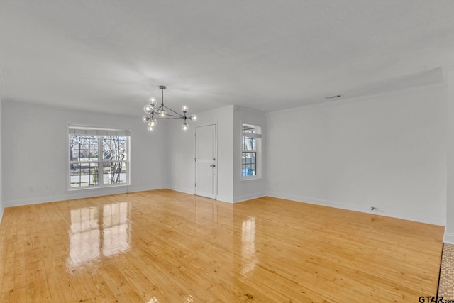 spare room featuring an inviting chandelier, crown molding, and light hardwood / wood-style floors