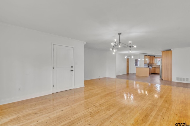 unfurnished room with an inviting chandelier, crown molding, and light wood-type flooring