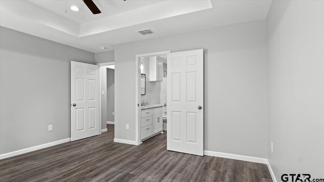 unfurnished bedroom with visible vents, ensuite bathroom, a tray ceiling, dark wood-style floors, and baseboards