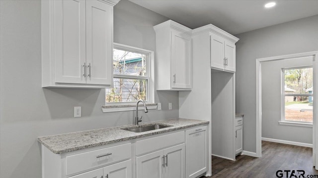 kitchen with dark wood-type flooring, a sink, light stone counters, white cabinets, and baseboards