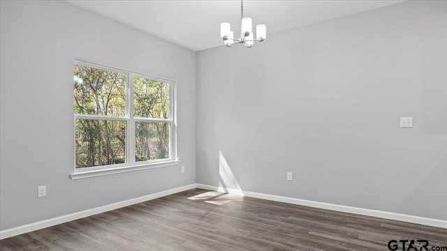 unfurnished room featuring dark wood finished floors, a notable chandelier, and baseboards