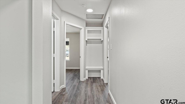 hall with wood finished floors, visible vents, and baseboards