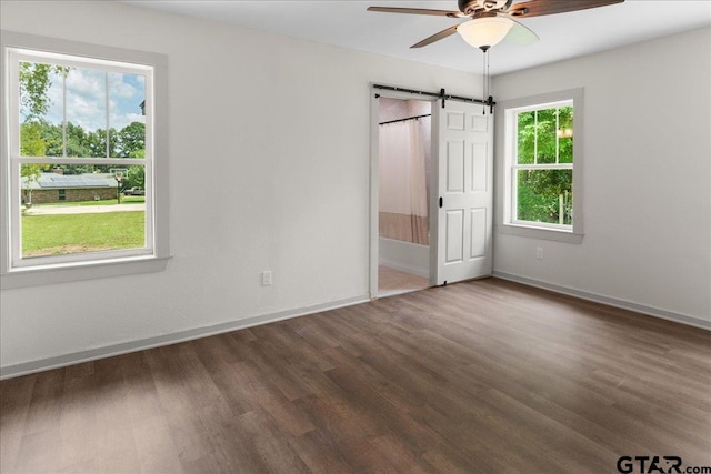 unfurnished bedroom featuring dark wood-type flooring, a barn door, and ceiling fan