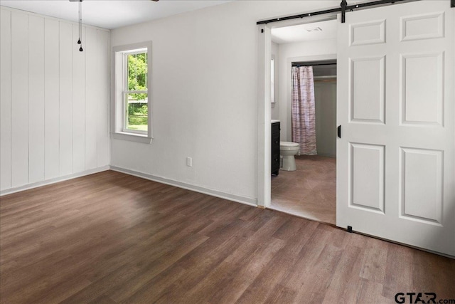 unfurnished bedroom with connected bathroom, wood-type flooring, and a barn door