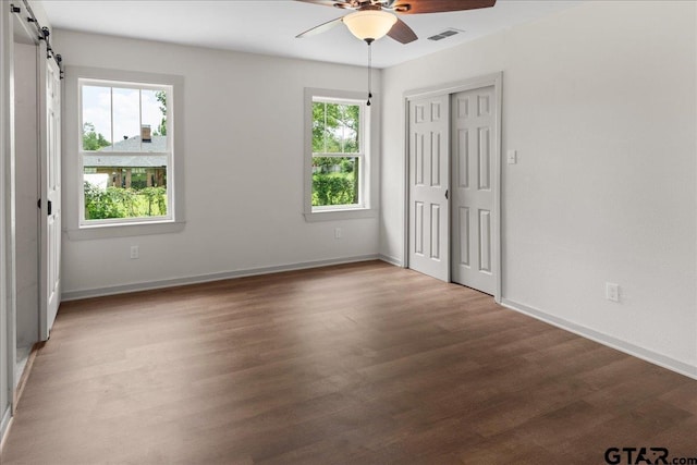 unfurnished bedroom with multiple windows, hardwood / wood-style floors, a barn door, and ceiling fan