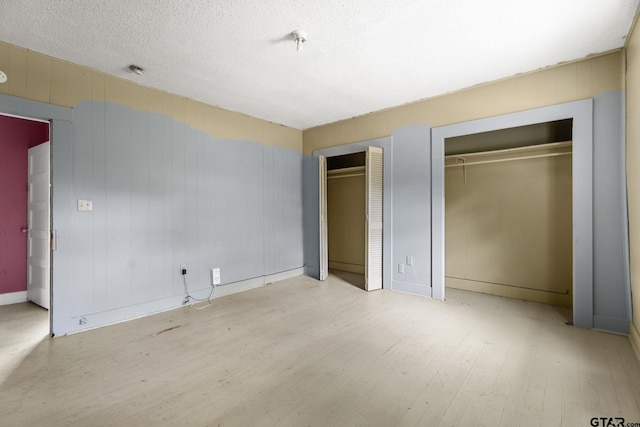 unfurnished bedroom featuring two closets, wood finished floors, baseboards, and a textured ceiling