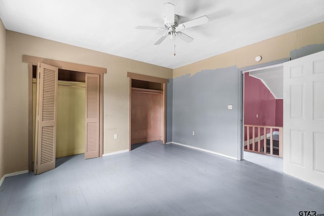 unfurnished bedroom with baseboards, a ceiling fan, multiple closets, and wood finished floors