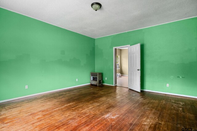 empty room featuring baseboards, heating unit, and wood finished floors