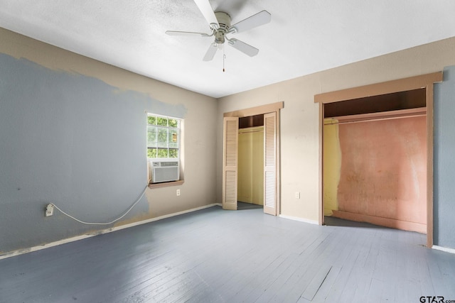 unfurnished bedroom featuring baseboards, cooling unit, hardwood / wood-style floors, and two closets