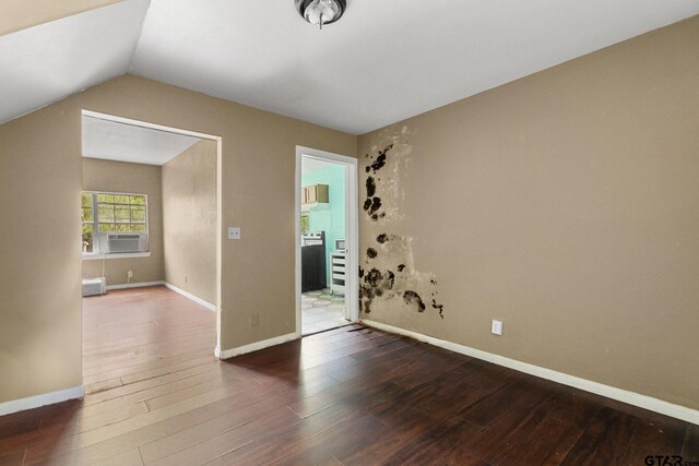 empty room featuring cooling unit, baseboards, lofted ceiling, and hardwood / wood-style floors