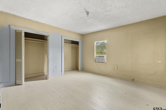 unfurnished bedroom featuring cooling unit, multiple closets, a textured ceiling, and wood finished floors