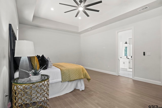 bedroom featuring wood-type flooring, ceiling fan, a raised ceiling, and connected bathroom