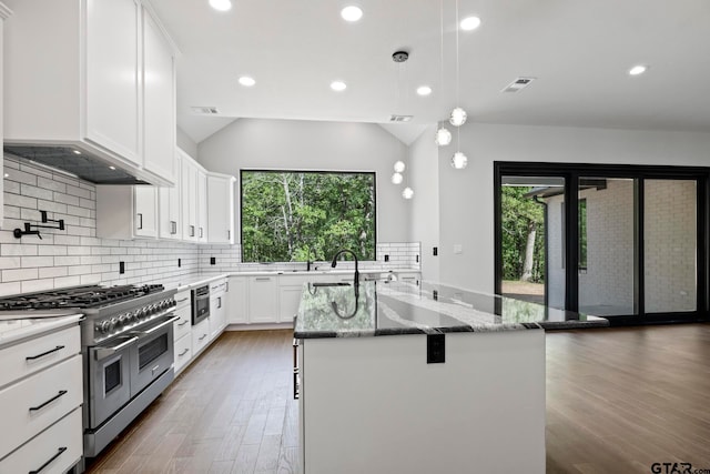 kitchen featuring light stone counters, a center island with sink, stainless steel appliances, dark hardwood / wood-style flooring, and white cabinets