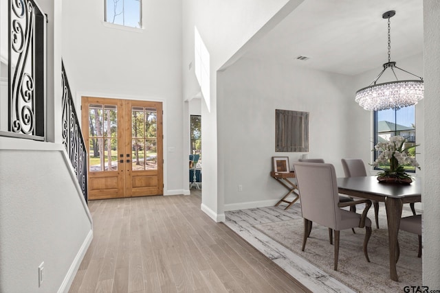 entryway with a high ceiling, french doors, a notable chandelier, and light hardwood / wood-style floors