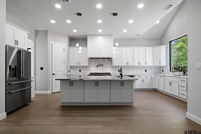 kitchen featuring high end refrigerator, a center island with sink, light stone counters, decorative light fixtures, and dark hardwood / wood-style flooring