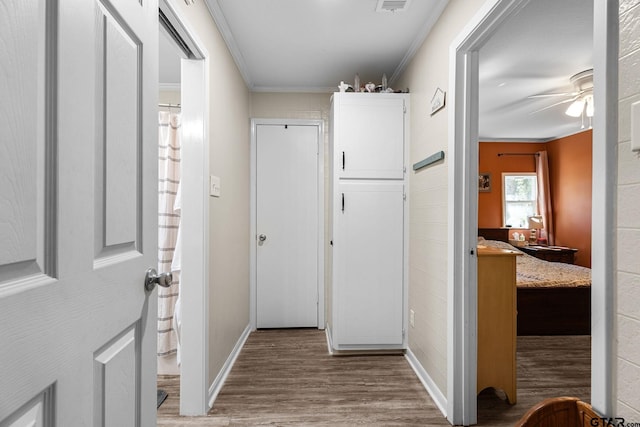 corridor with ornamental molding and light hardwood / wood-style flooring