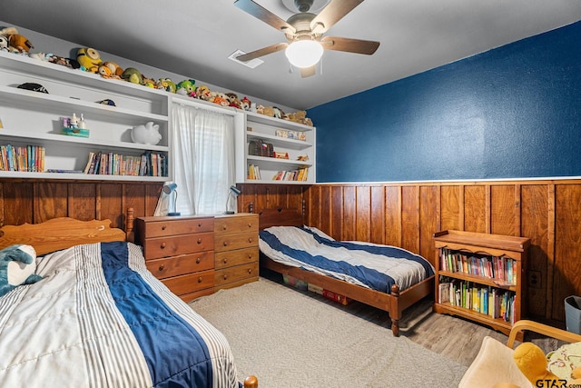 bedroom featuring light hardwood / wood-style floors, wood walls, and ceiling fan