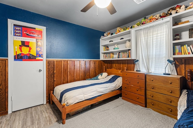 bedroom featuring light wood-type flooring, wood walls, and ceiling fan