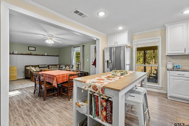 kitchen with a wealth of natural light, white cabinetry, stainless steel refrigerator with ice dispenser, and ceiling fan