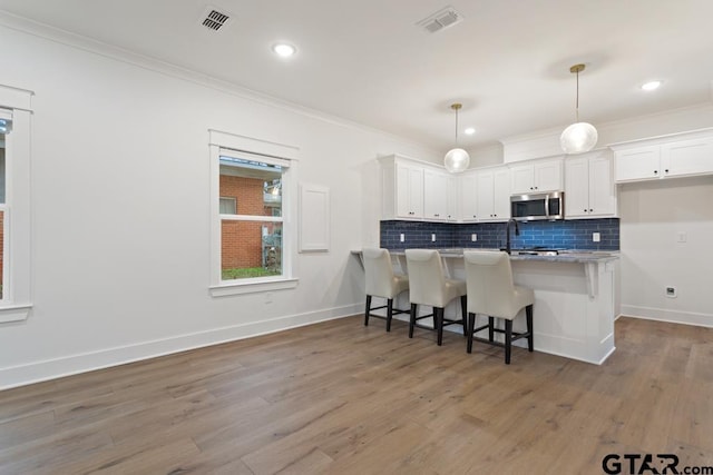 kitchen with hanging light fixtures, decorative backsplash, a kitchen breakfast bar, and white cabinets