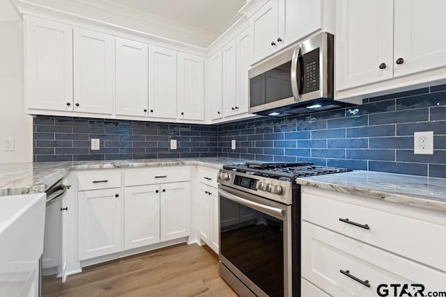 kitchen with light stone countertops, light hardwood / wood-style flooring, stainless steel appliances, and white cabinets