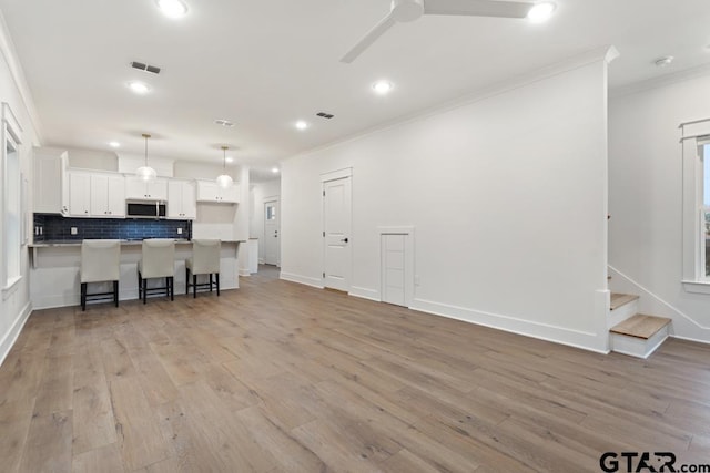 kitchen featuring a breakfast bar area, tasteful backsplash, hanging light fixtures, ornamental molding, and white cabinets