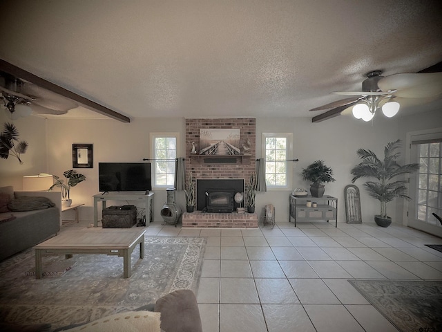 tiled living room with beamed ceiling, a textured ceiling, ceiling fan, and a brick fireplace