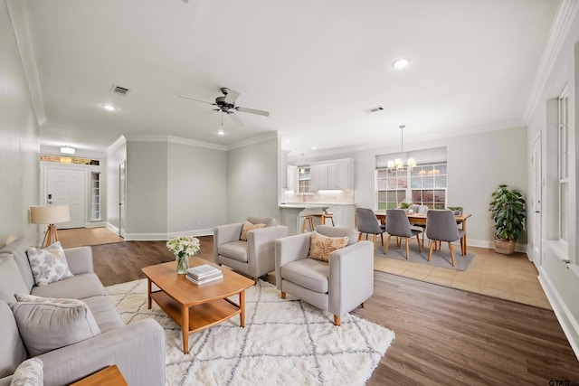 living room with ceiling fan with notable chandelier, light wood-type flooring, and ornamental molding