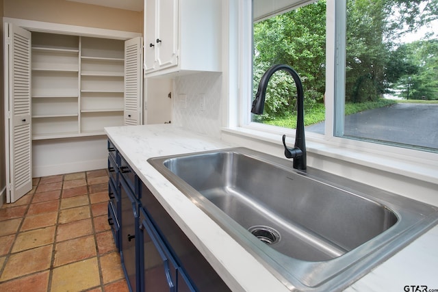 kitchen with white cabinetry, blue cabinets, light stone countertops, and a sink