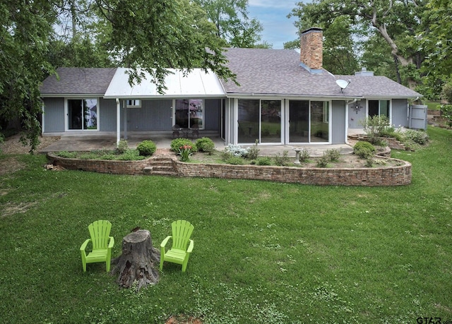 rear view of property with a chimney, a patio, roof with shingles, and a lawn