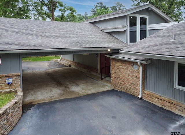 view of property exterior with driveway, an attached carport, a shingled roof, and brick siding