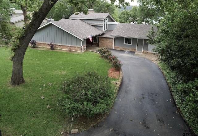 view of front of property with driveway, board and batten siding, a chimney, roof with shingles, and a front yard