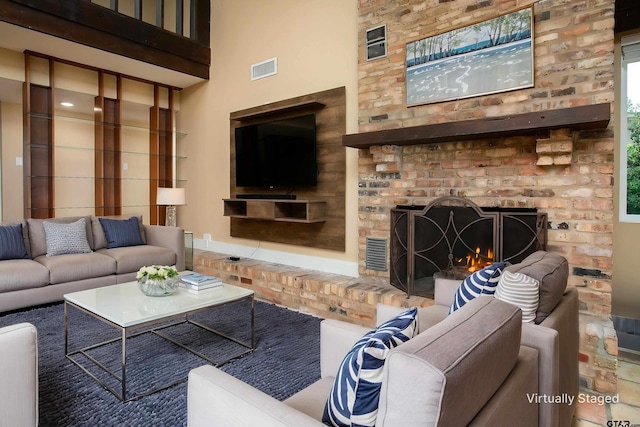 living area featuring a towering ceiling, visible vents, and a brick fireplace