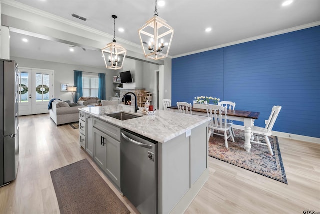 kitchen with a center island with sink, stainless steel appliances, hanging light fixtures, sink, and light hardwood / wood-style flooring