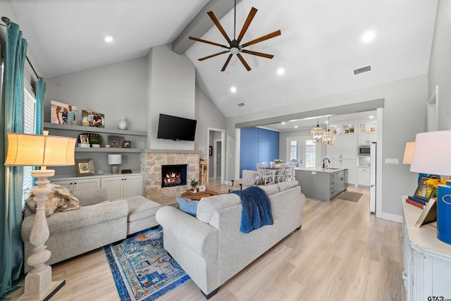 living room featuring beamed ceiling, sink, light hardwood / wood-style floors, and ceiling fan with notable chandelier