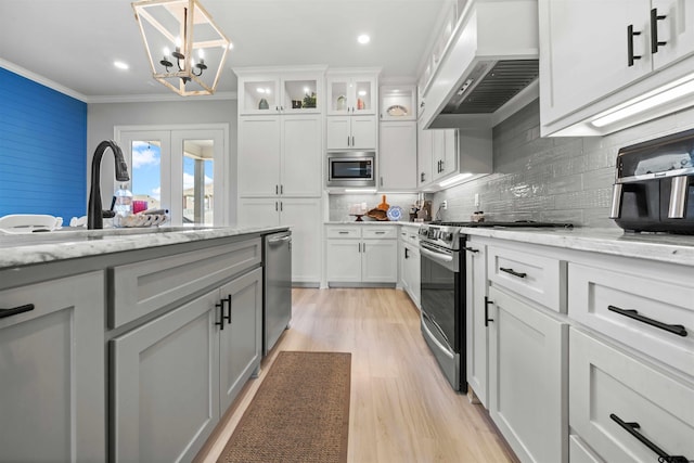 kitchen with stainless steel appliances, crown molding, custom range hood, light stone countertops, and white cabinets