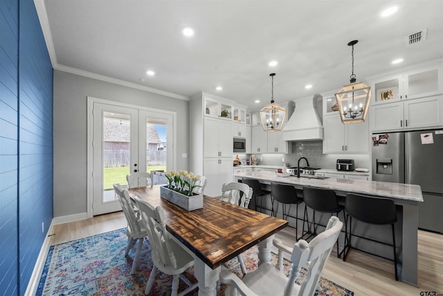 dining space with an inviting chandelier, french doors, crown molding, and light hardwood / wood-style flooring