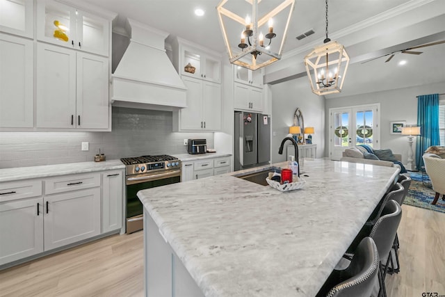 kitchen with sink, custom exhaust hood, white cabinetry, light wood-type flooring, and appliances with stainless steel finishes