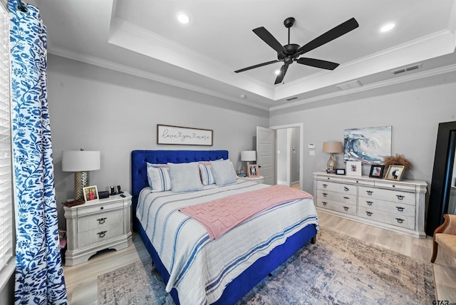 bedroom featuring light hardwood / wood-style flooring, ceiling fan, crown molding, and a tray ceiling