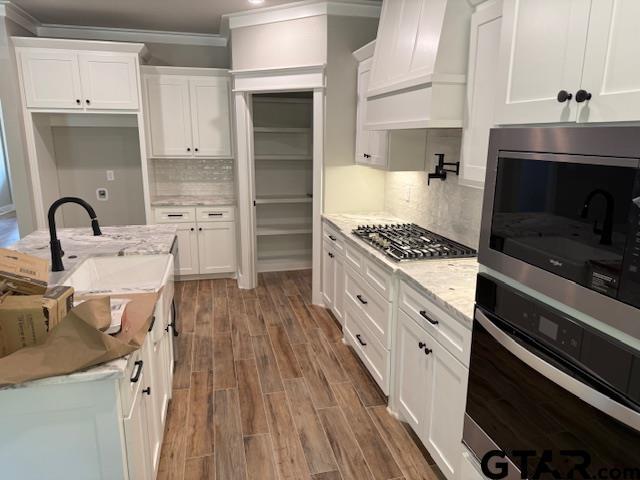 14533 Woodland Creek Dr, Tyler, TX 75706 - kitchen with custom exhaust hood, stainless steel appliances, ornamental molding, and white cabinetry