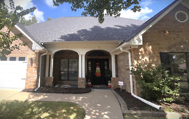 view of exterior entry featuring stone siding, roof with shingles, and an attached garage