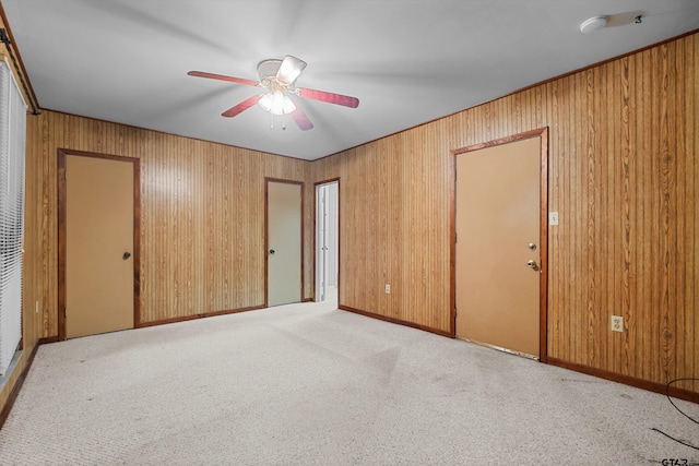 unfurnished room featuring light carpet, wood walls, and a ceiling fan