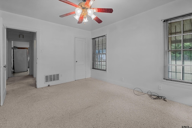 unfurnished room with light carpet, visible vents, and a ceiling fan