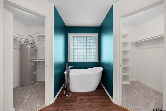 bathroom featuring built in shelves, a textured ceiling, a tub, and water heater