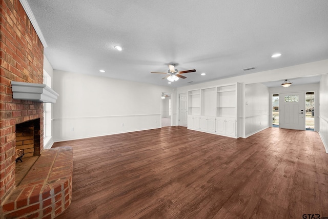 unfurnished living room with hardwood / wood-style floors, a brick fireplace, built in shelves, ceiling fan, and a textured ceiling