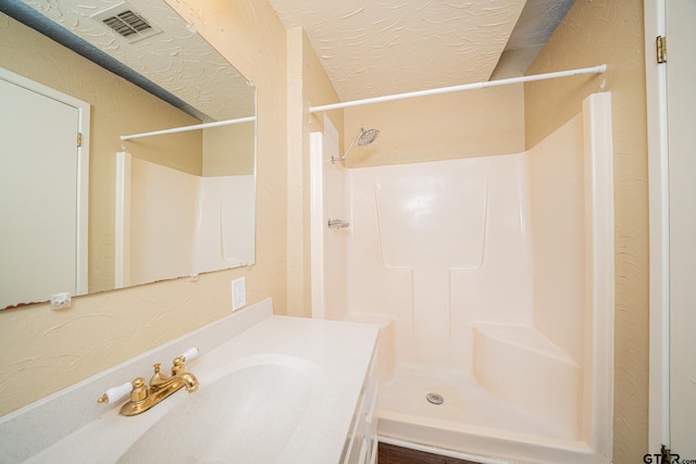 bathroom with a textured ceiling, walk in shower, and vanity