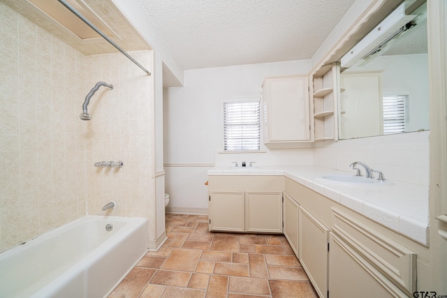 full bathroom with toilet, vanity, a textured ceiling, and tiled shower / bath