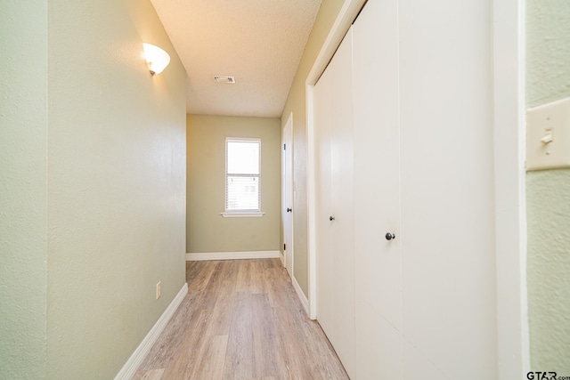 hallway with a textured ceiling and light hardwood / wood-style floors